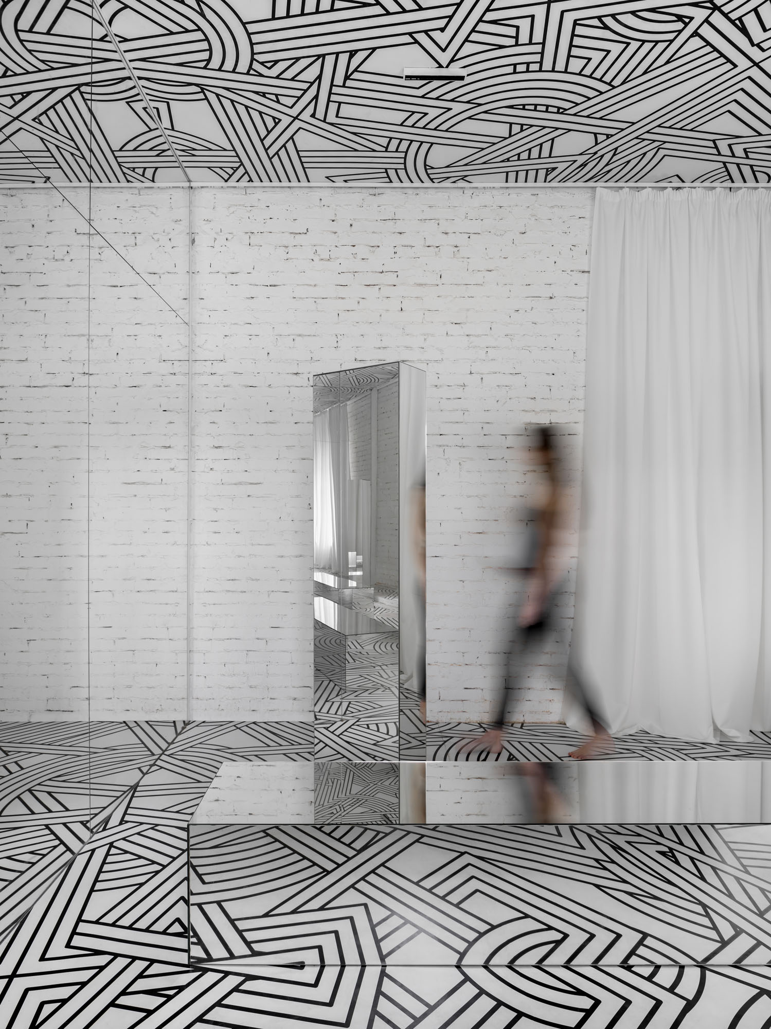 a woman walking past mirrored objects in a hallway with a graphic on the ceiling and floor
