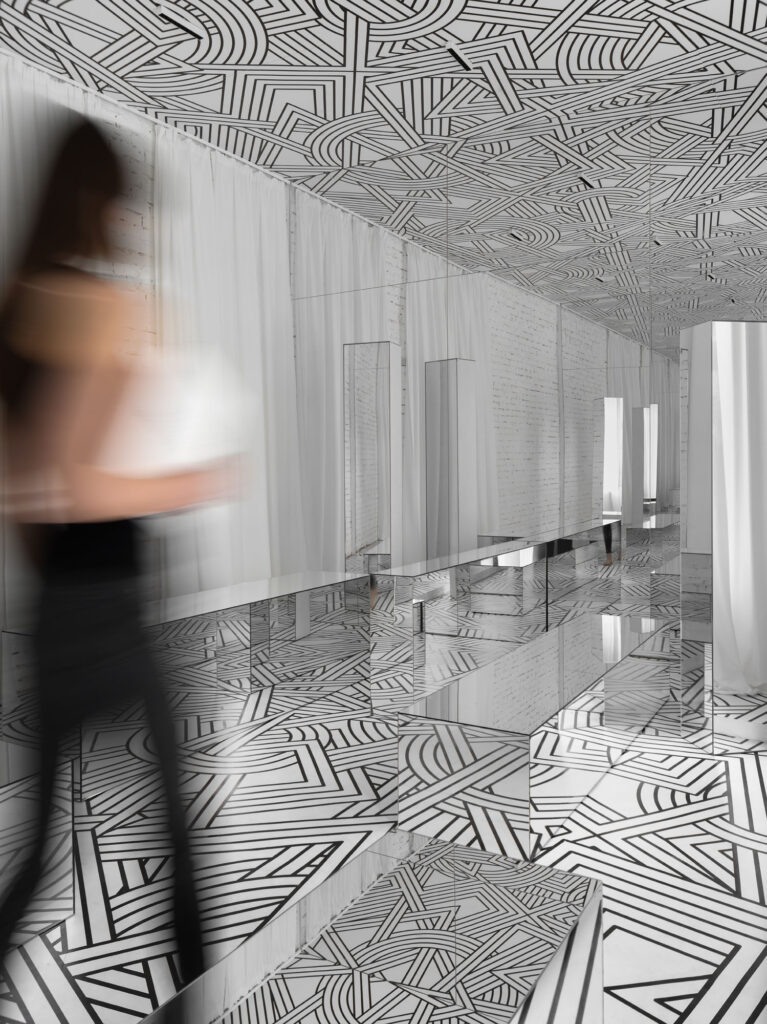 a woman walks through mirrored surfaces in a hallway with graphic on the floor and ceiling
