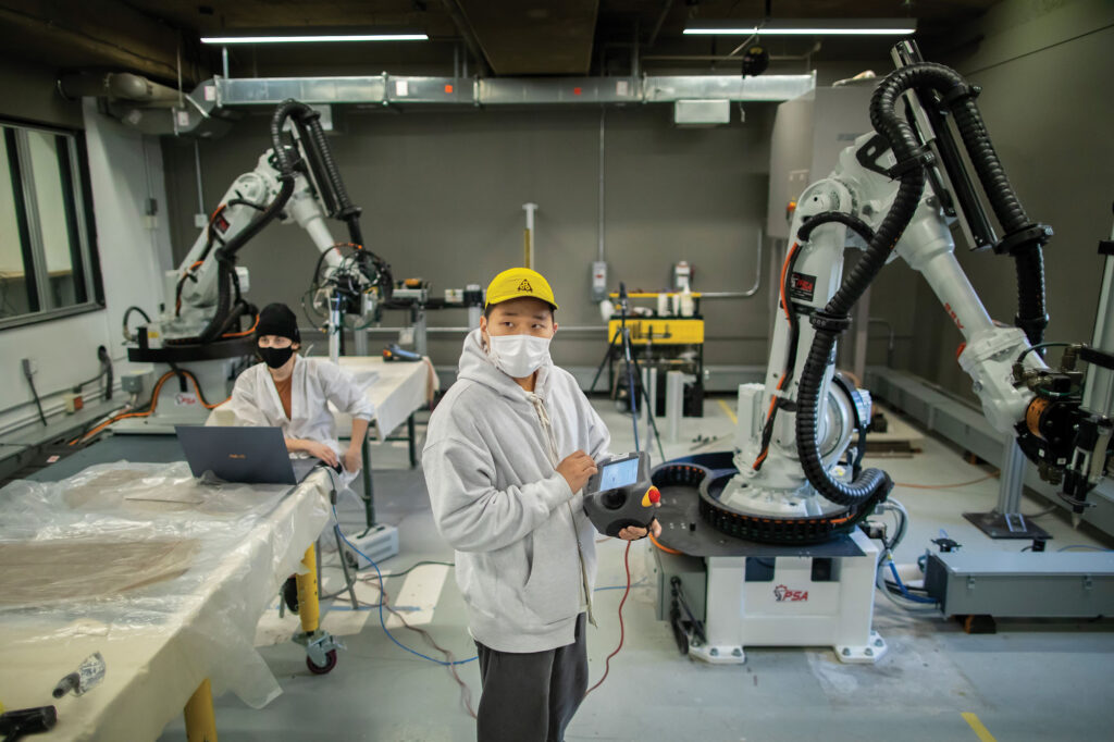 student standing before fabrication robots