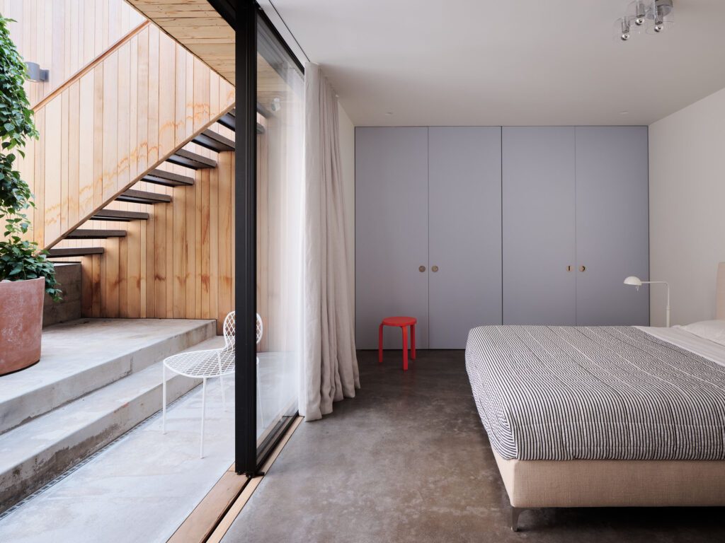 interior image of a bedroom with sliding glass doors that look out onto a courtyard with plants and exterior stairs