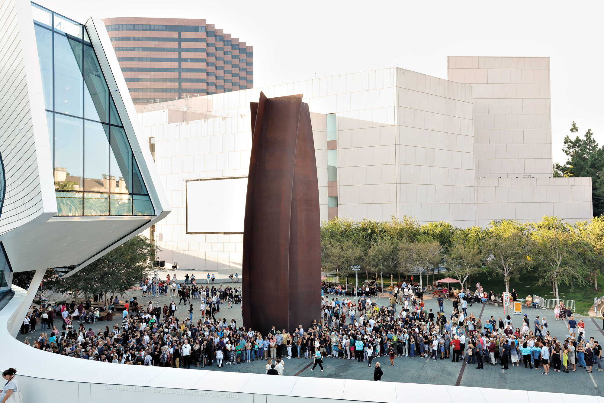 Exterior image of a courtyard with visitors surrounding a richard serra sculpture. 