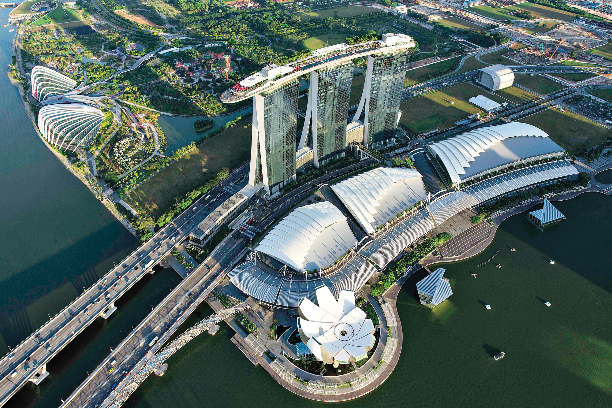 An aerial photograph of the Marina Bay Sands hotel and skypark designed by Moshe Safdie in Singapore that depicts lush gardens on the roof