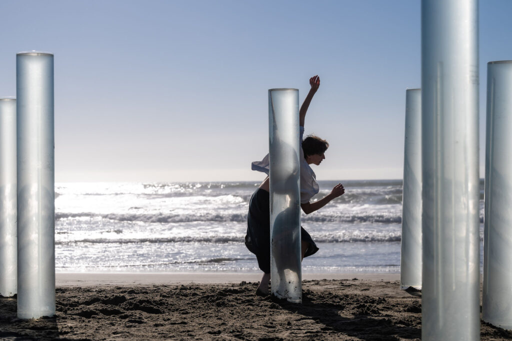 a woman dancing on a beach surrounded by clear cylinders filled with sea water