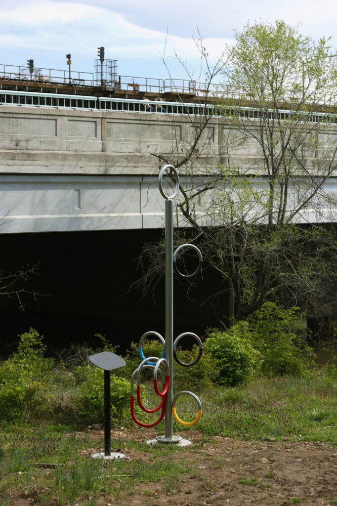 a sculpture located by a river that flows under a highway overpass