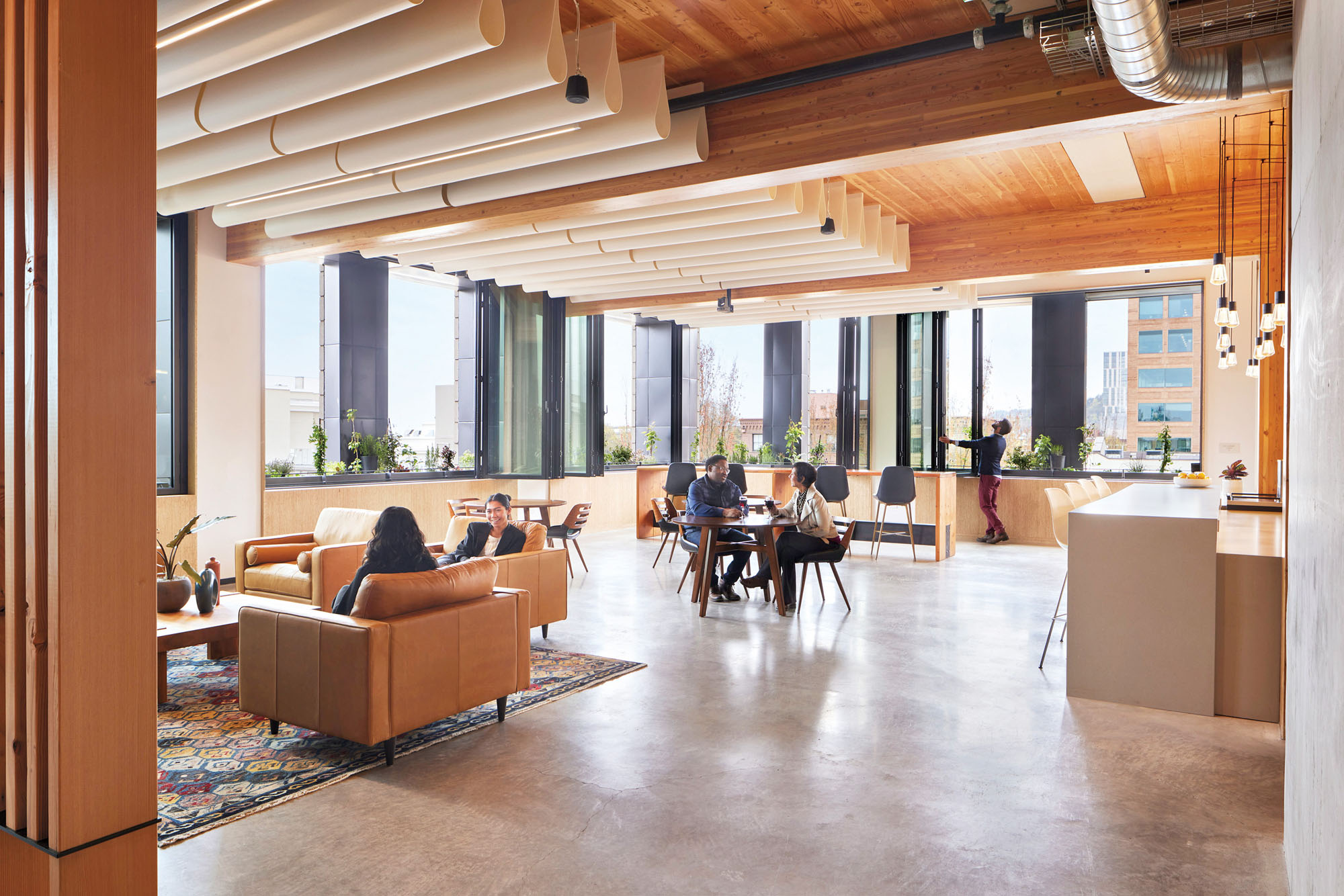 A photograph of the interior of a workplace, workers are sitting at casual tables, and mass timber construction is visible 