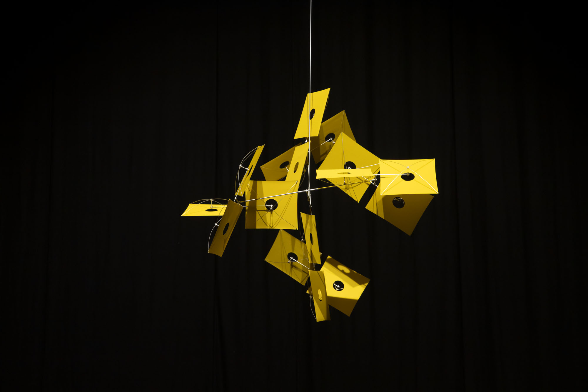 a yellow sculpture by Susumu Shingu suspended in front of a black background