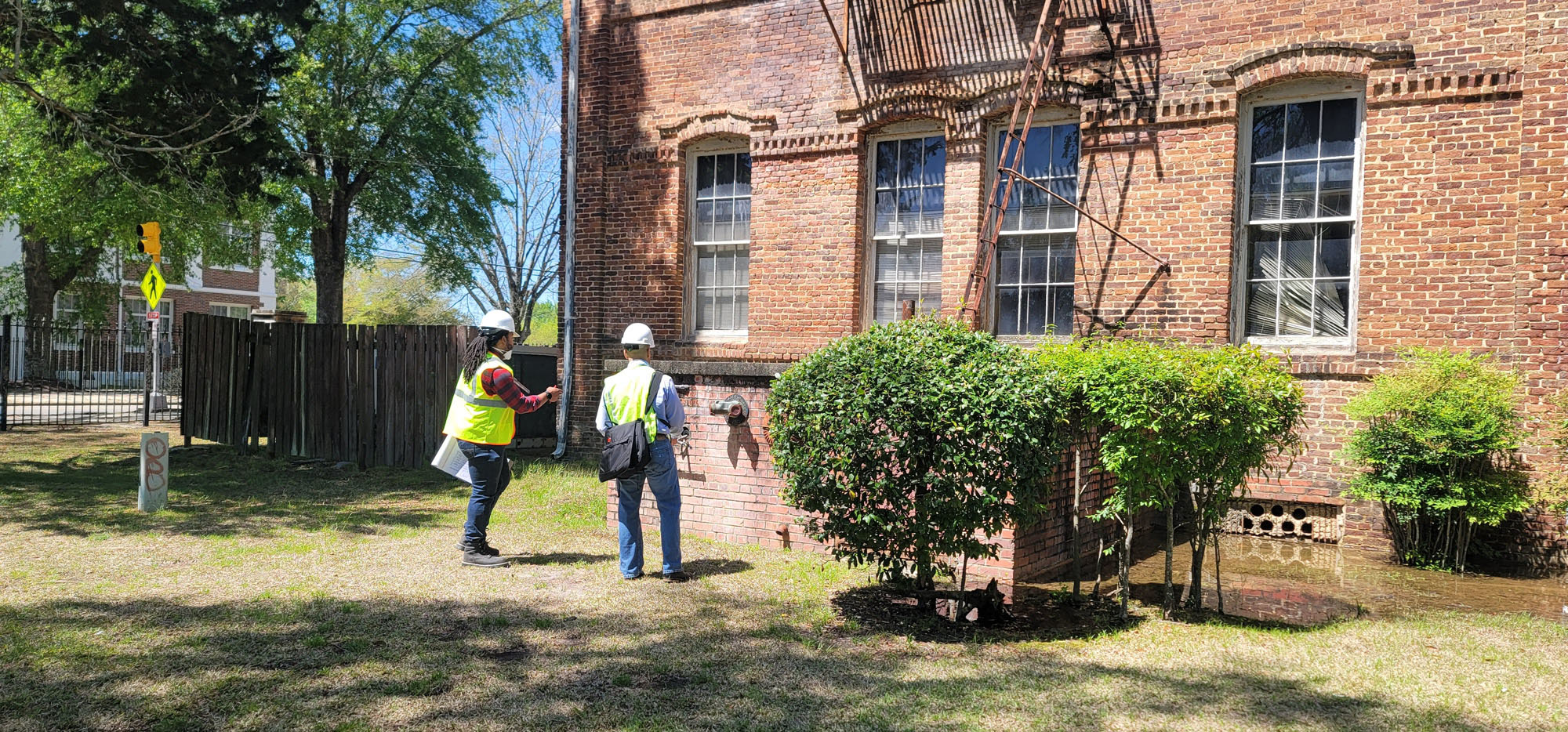 a photograph of two people with reflective vests investigating a brick building