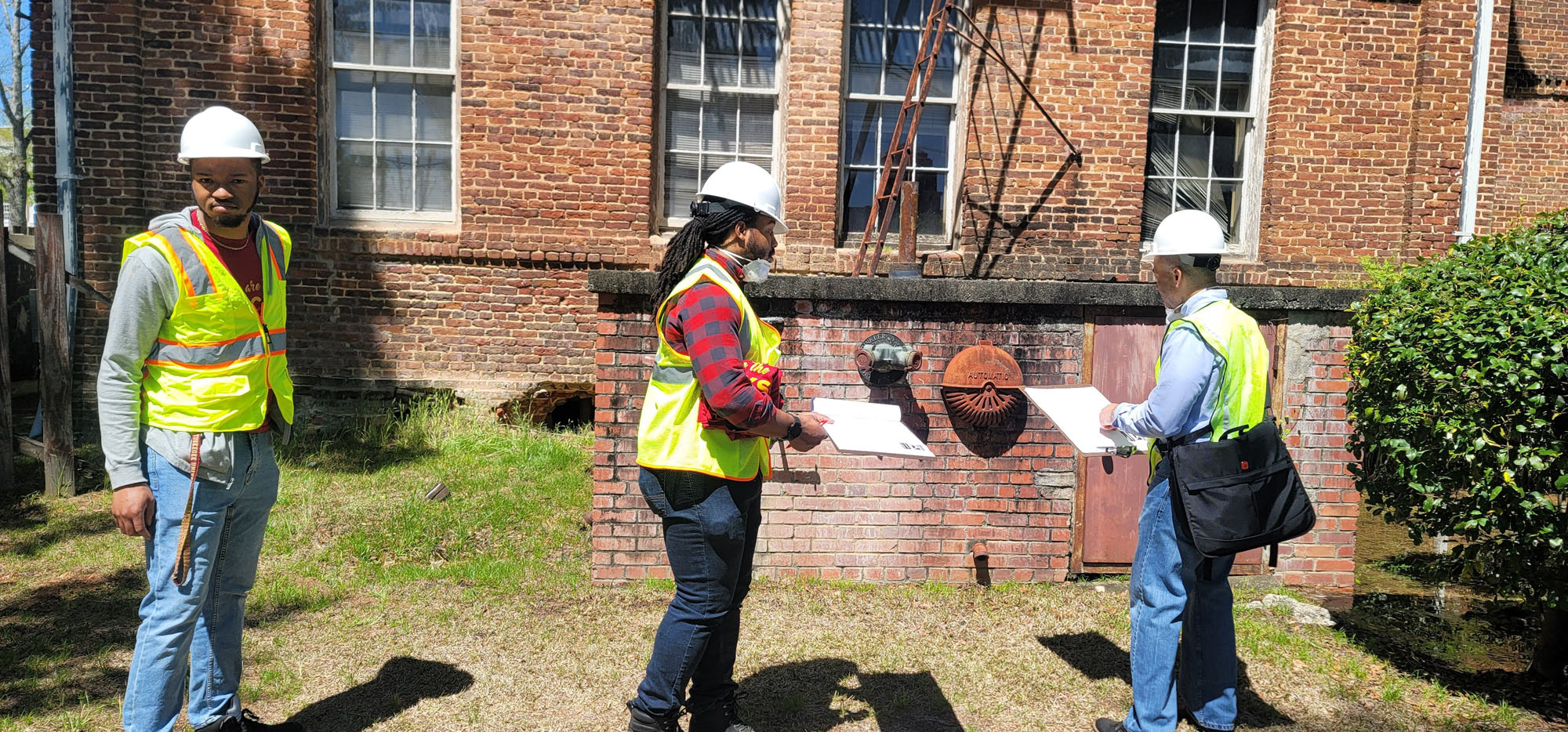 a photograph of three people in reflective vests inspecting a brick building