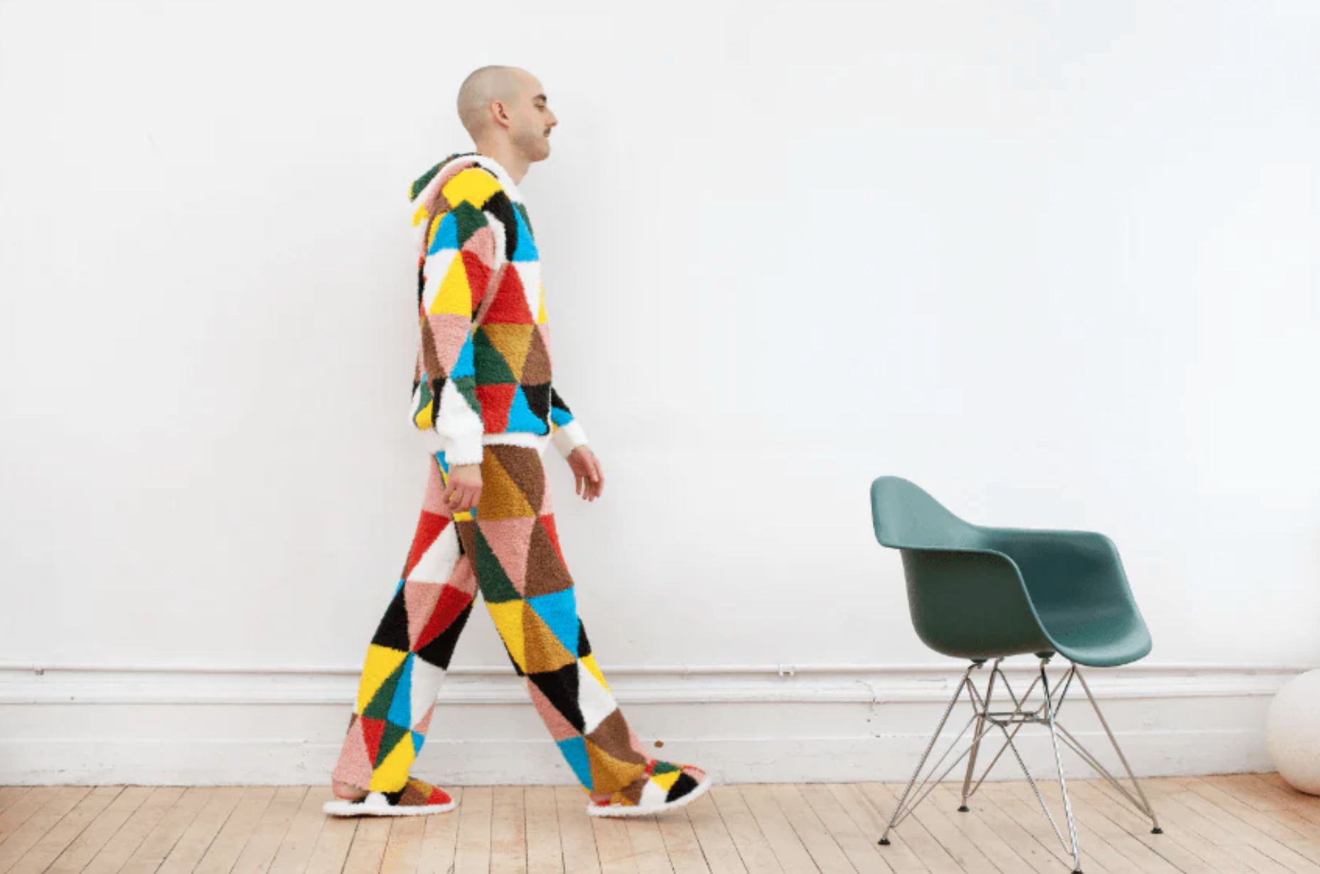 an image of a person in colorful loungewear walking towards an eames chair